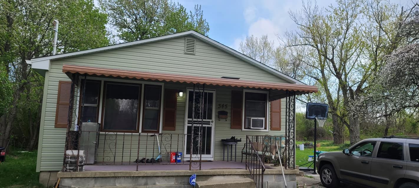 Small gray house with a front porch, red shutters, and a parked SUV in the yard.
