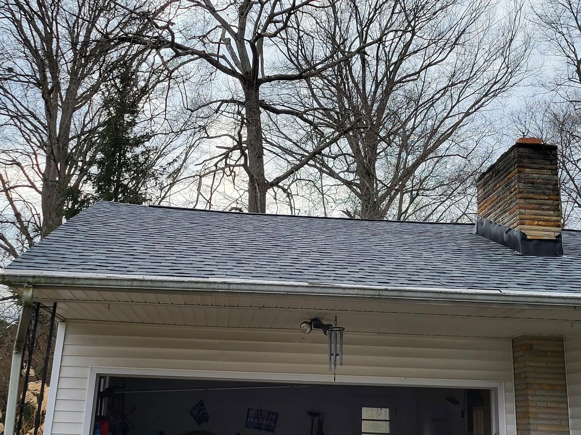 Snow-covered garage roof with a brick chimney and bare trees in the background