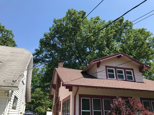 Residential houses with red siding and white trim under a blue sky, with trees and power lines overhead