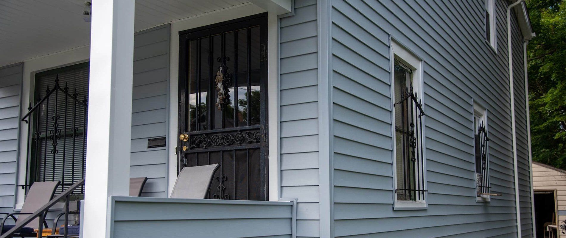 White house exterior with gray siding, barred windows, and a small porch railing
