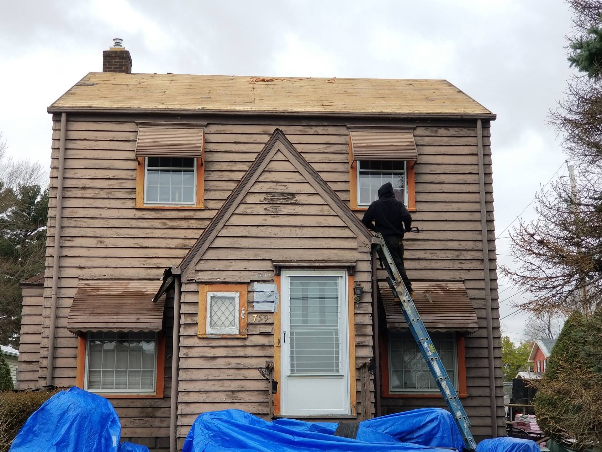 Person on ladder repairing the upper window of a small wooden house