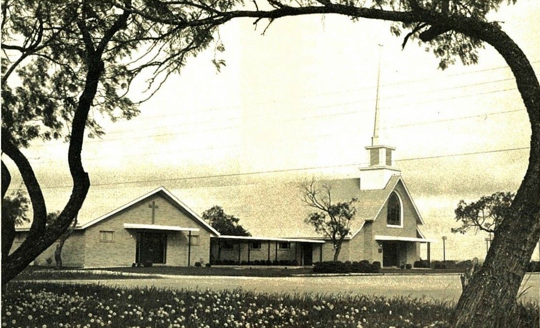 A black and white photo of a church surrounded by trees