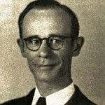 A man wearing glasses and a suit and tie is smiling in a black and white photo.