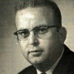 A black and white photo of a man wearing glasses and a suit and tie.