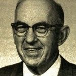 A man wearing glasses and a suit is smiling in a black and white photo.