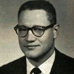 A black and white photo of a man wearing glasses and a suit and tie.