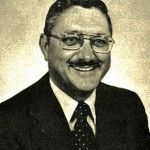 A man in a suit and tie is smiling in a black and white photo.