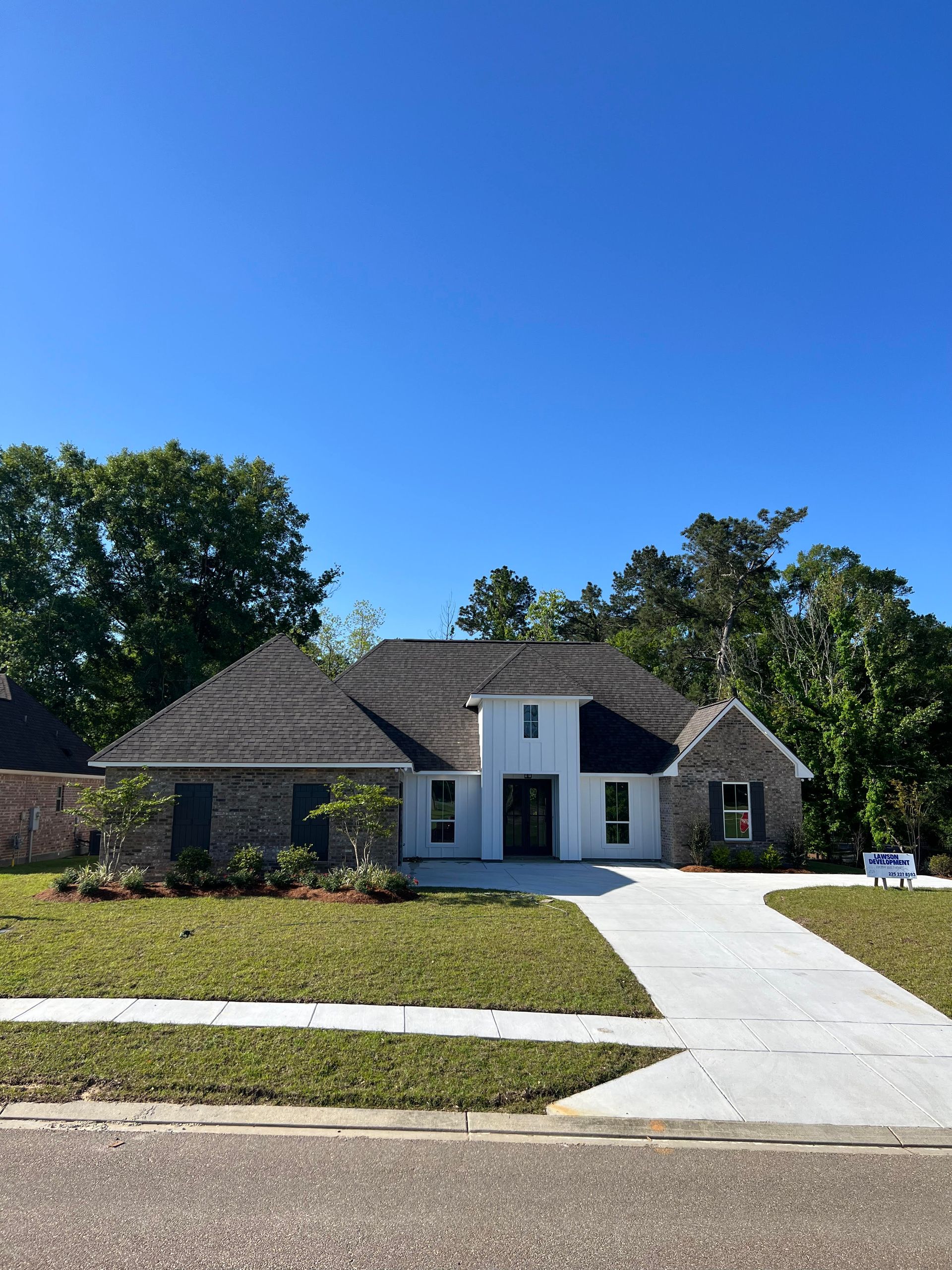 A large white house with a black roof is sitting on top of a lush green lawn.