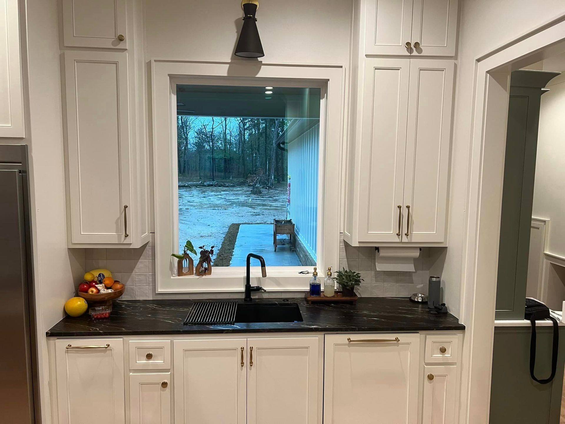 A kitchen with white cabinets , a sink , and a window.