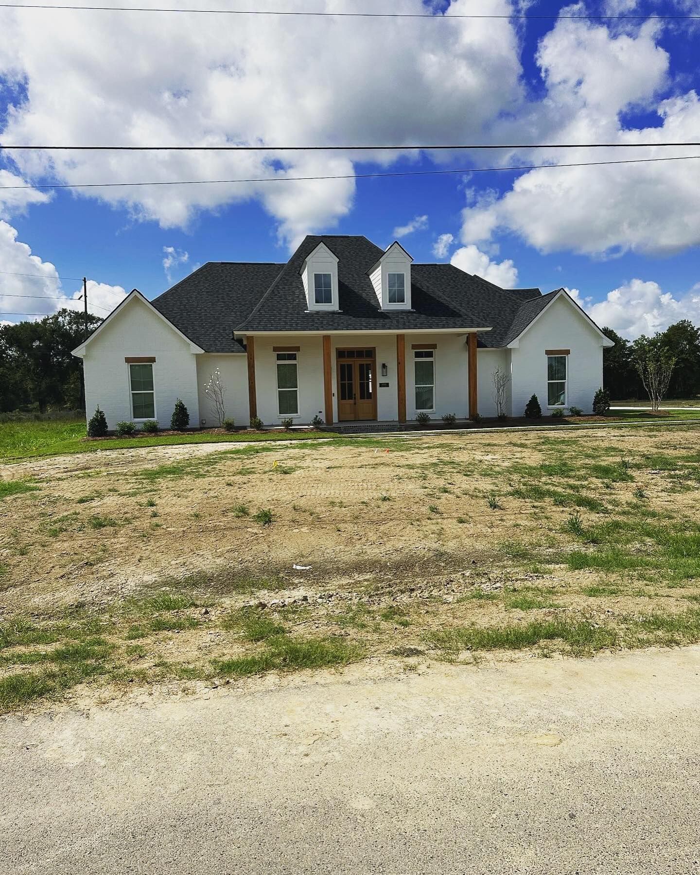 A white house with a black roof is sitting on top of a dirt field.
