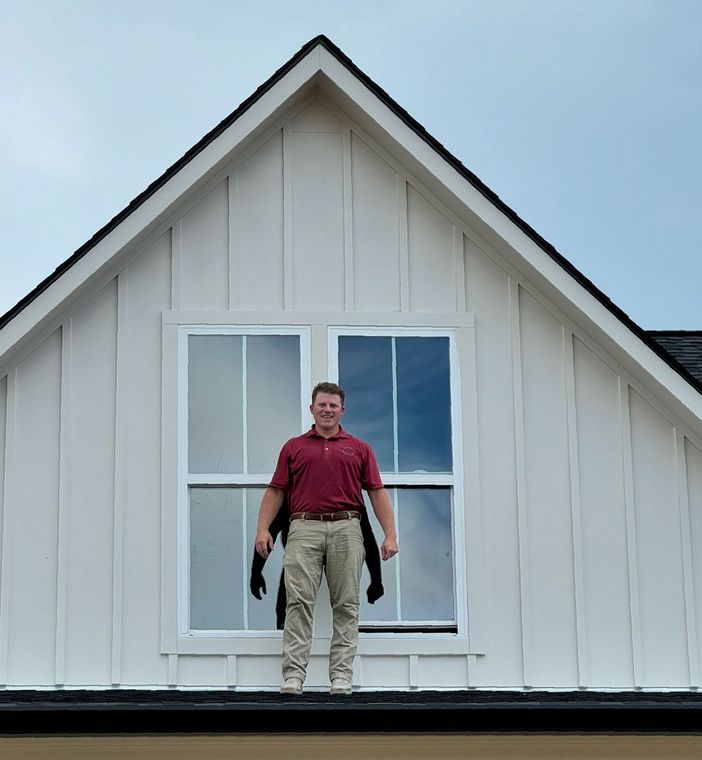 A man in a red shirt is standing on the roof of a white house