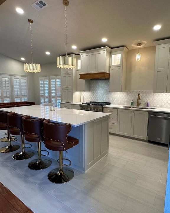 A kitchen with white cabinets , a large island , and stools.