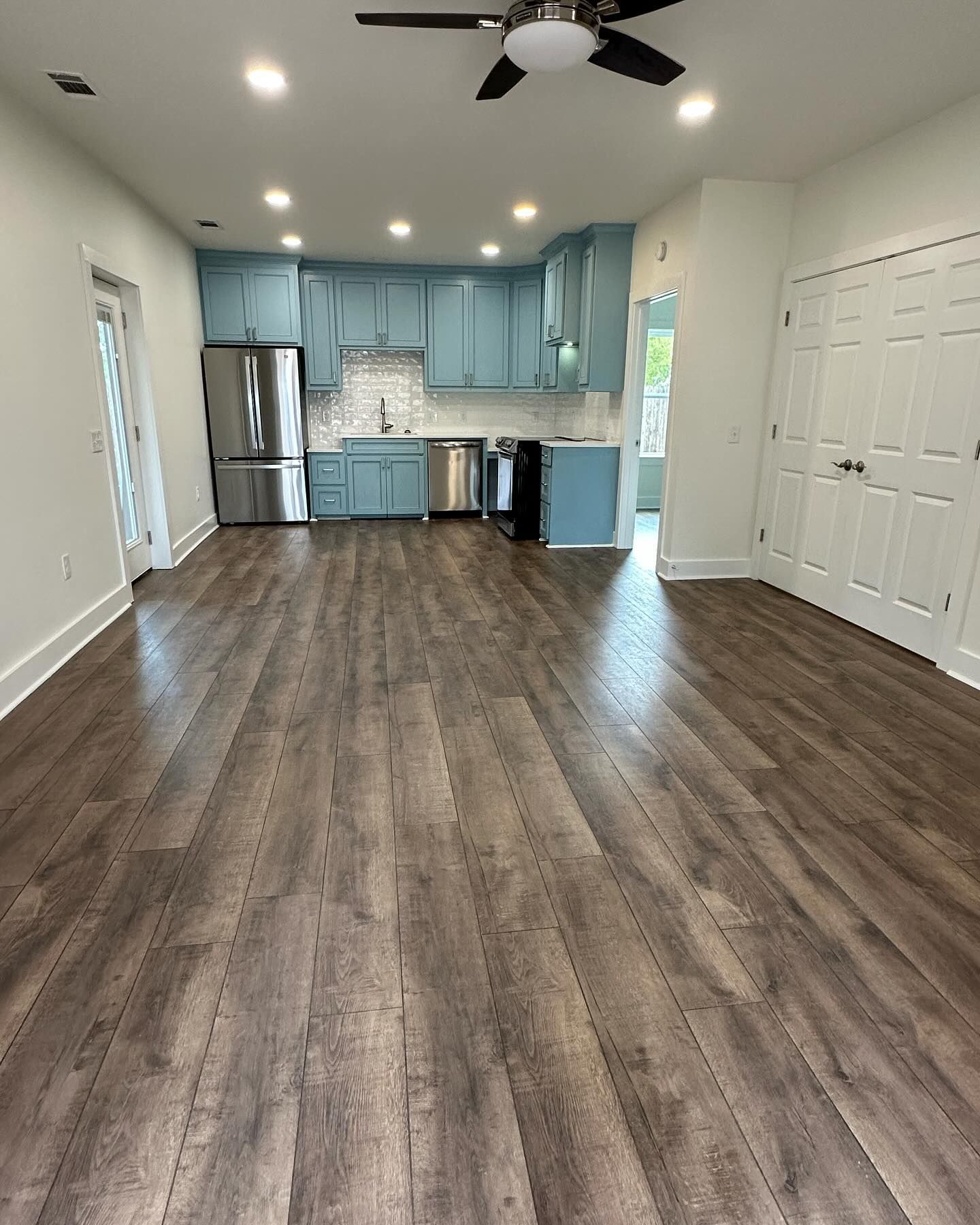 A kitchen with blue cabinets , stainless steel appliances , and a ceiling fan.