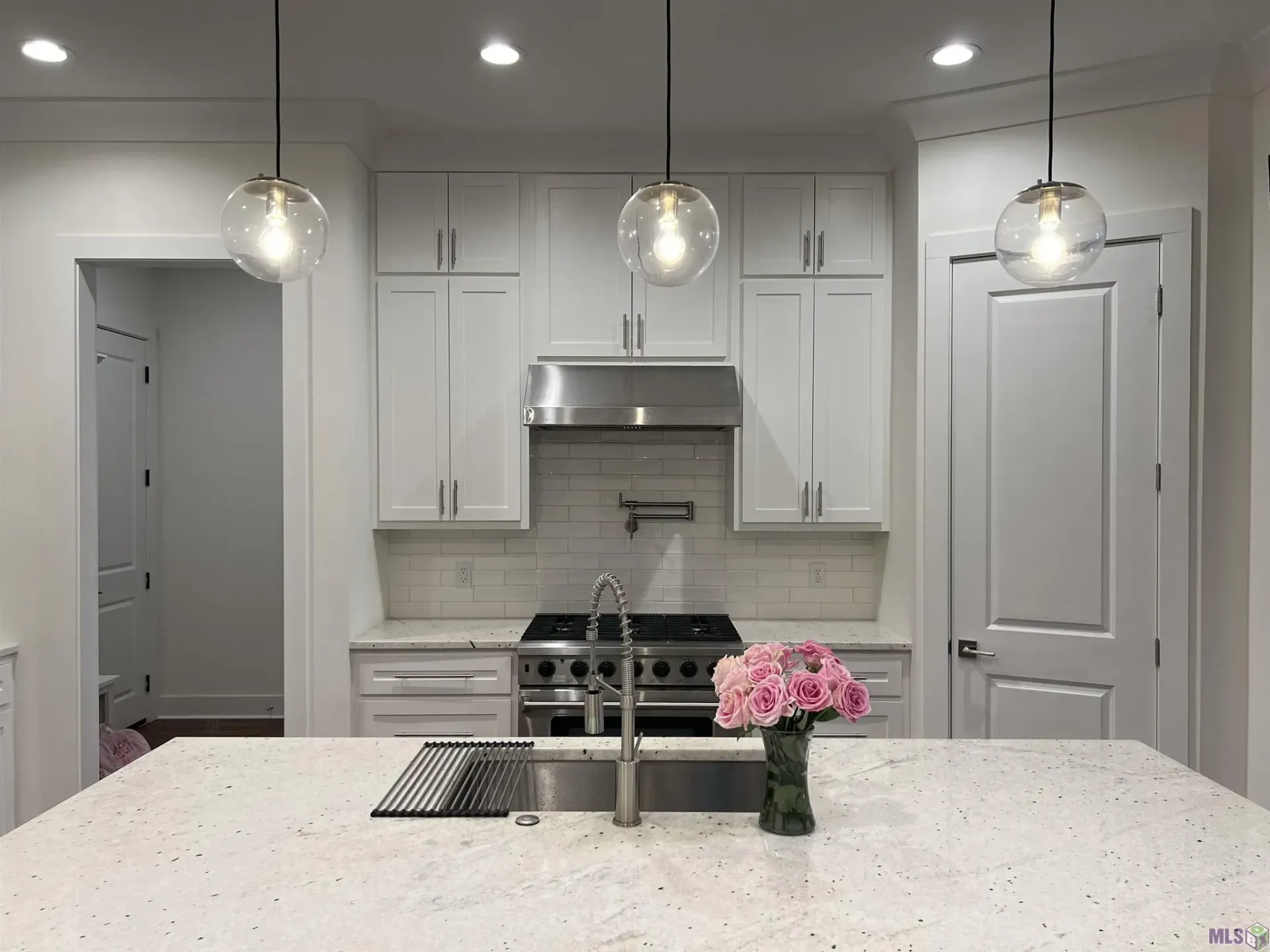 A kitchen with white cabinets , a sink , a stove , and a vase of flowers on the counter.