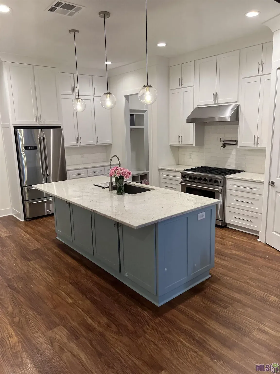 A kitchen with white cabinets , stainless steel appliances , and a large island.