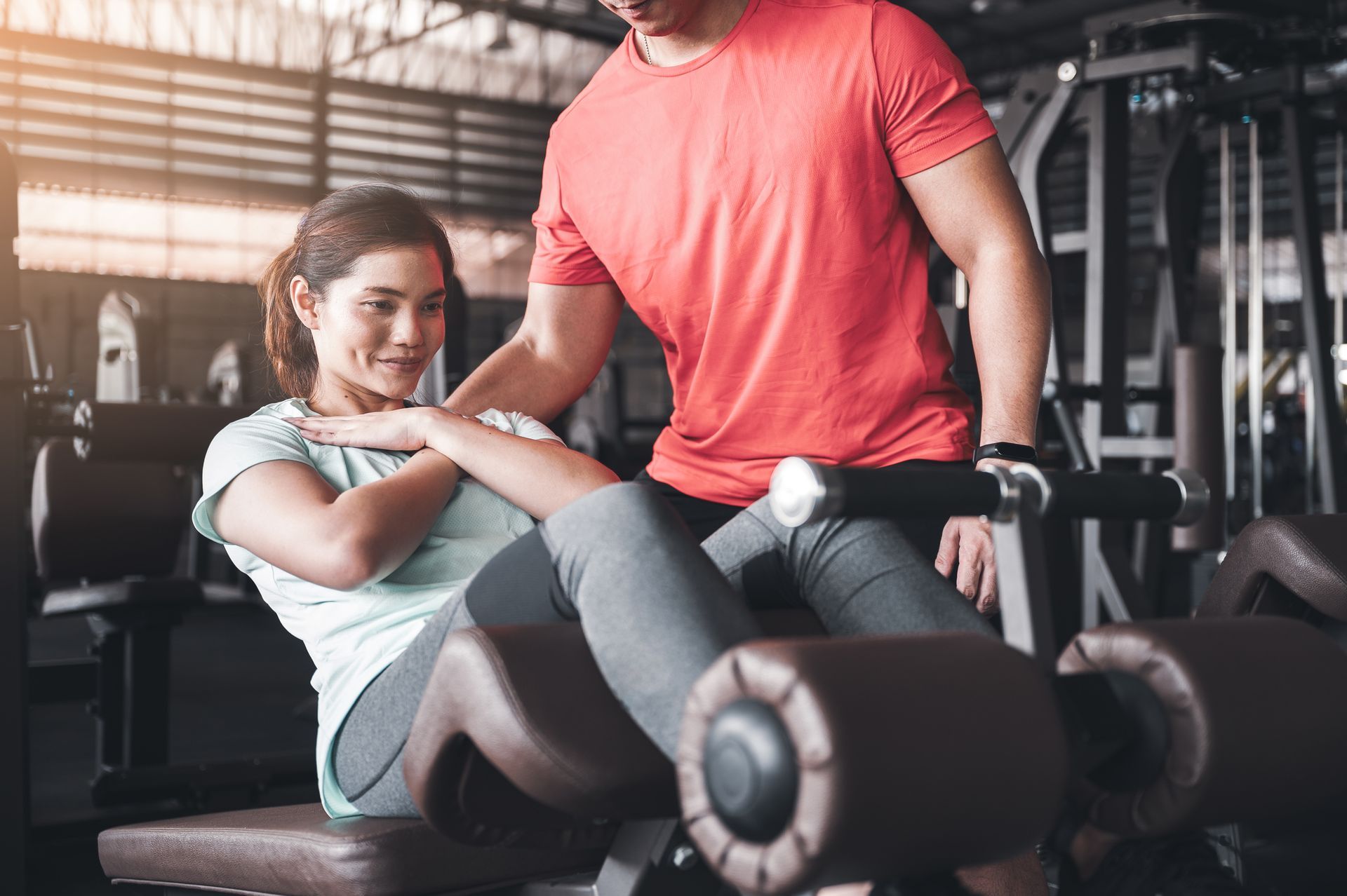 Una donna esegue gli addominali con l'aiuto di un personal trainer in palestra, aiutandosi con le mani sui piedi.