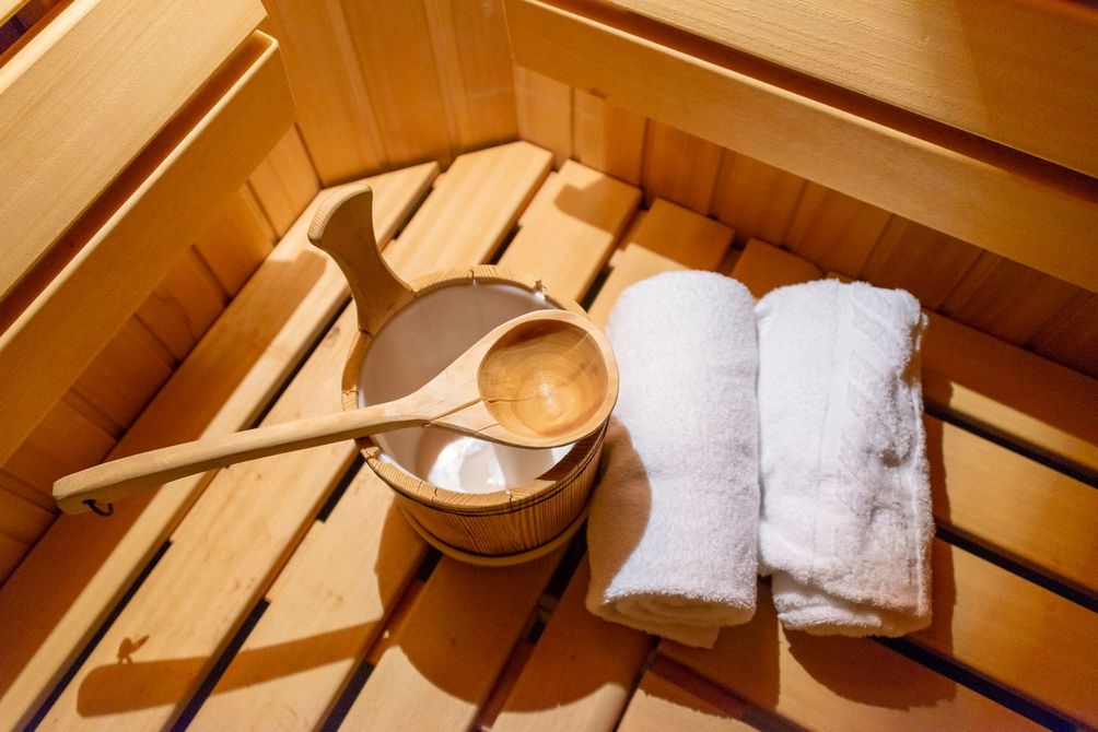 Interno della sauna in legno con secchio, mestolo e asciugamani bianchi arrotolati.