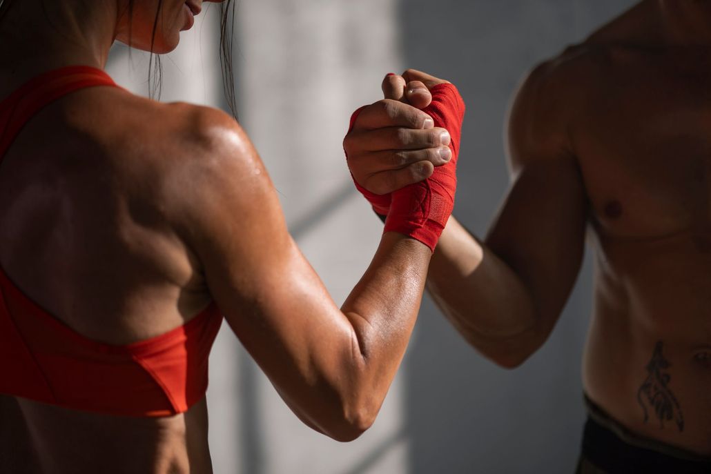 Due persone, una con un reggiseno sportivo rosso e delle fasce rosse per le mani, che si tengono per mano.
