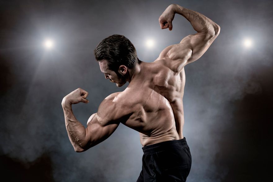 Uomo muscoloso che flette i bicipiti in un ambiente buio, sotto luci intense.