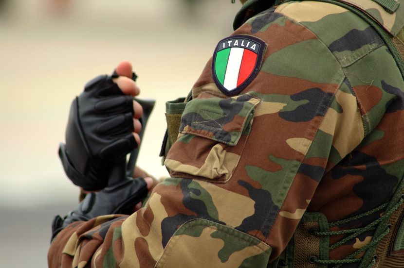 Soldato italiano in uniforme mimetica, braccio alzato, con toppa con bandiera italiana.