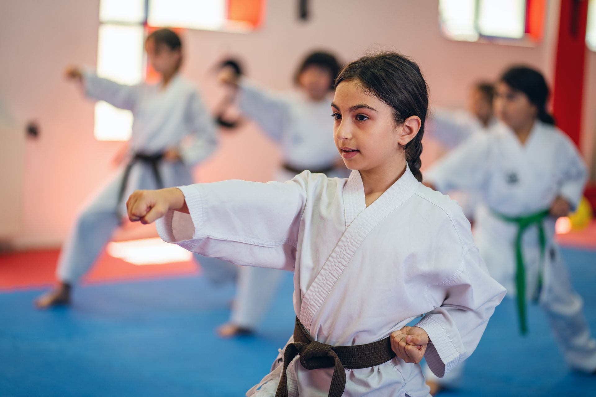 Bambini in uniforme bianca da karate si esercitano con i pugni, sul tappeto blu, uno in primo piano.