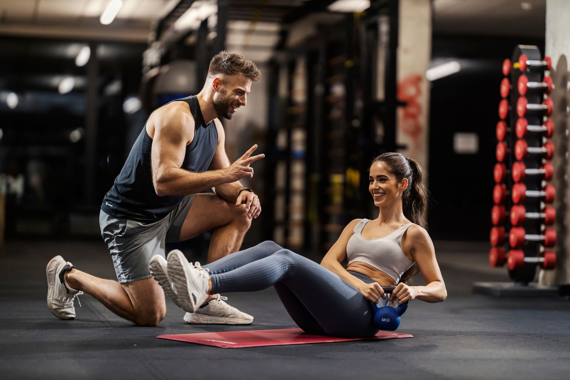 Un personal trainer aiuta una donna a eseguire sit-up con kettlebell in palestra.