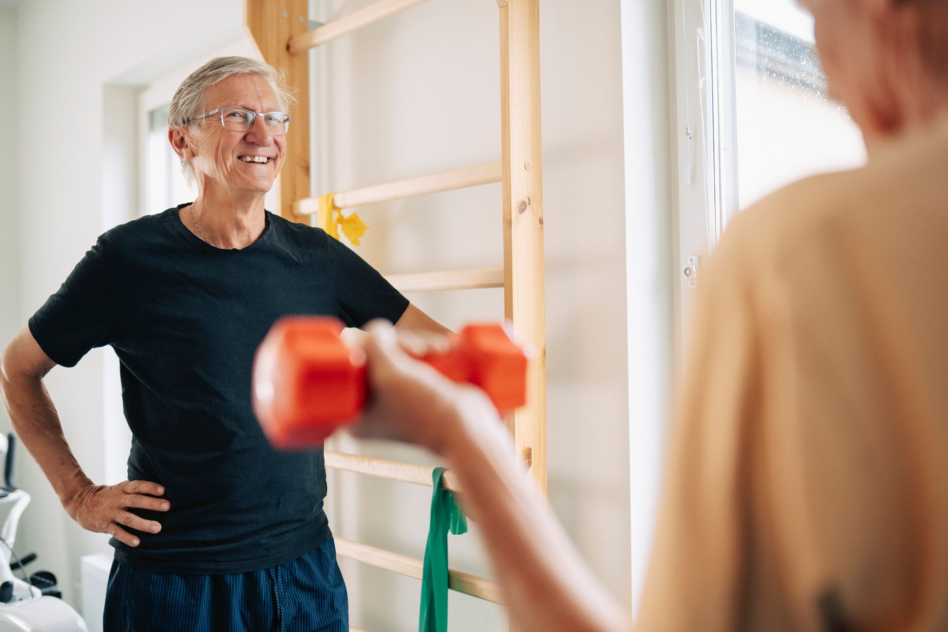 Un uomo osserva un'altra persona sollevare un piccolo manubrio rosso in una stanza con attrezzi ginnici.