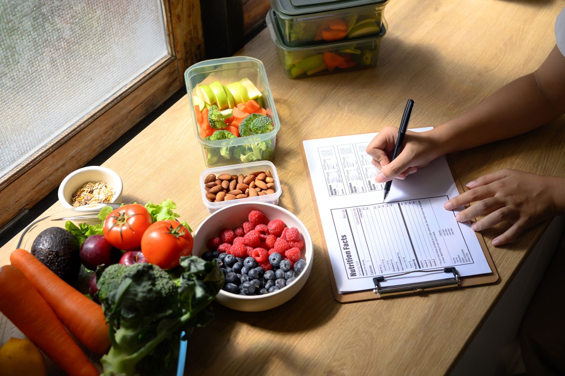Persona che scrive su un blocco appunti accanto al cibo preparato: verdura, frutta, noci in contenitori.