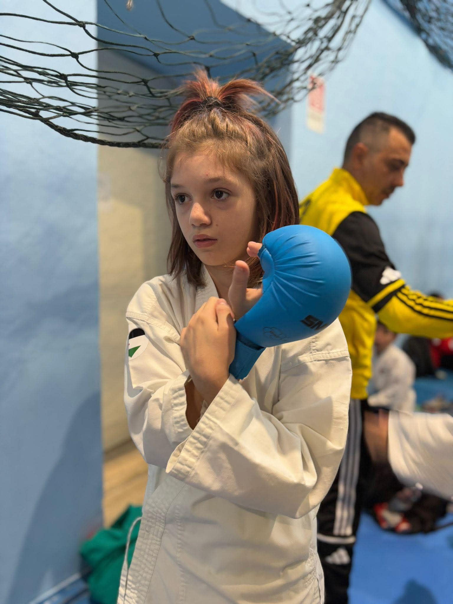 Giovane karateka in uniforme bianca e guanto blu, in piedi in una palestra.