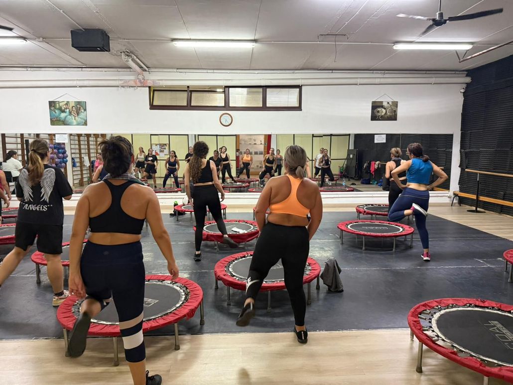 Persone che si allenano su mini trampolini in palestra. Gli specchi alle pareti riflettono l'allenamento.