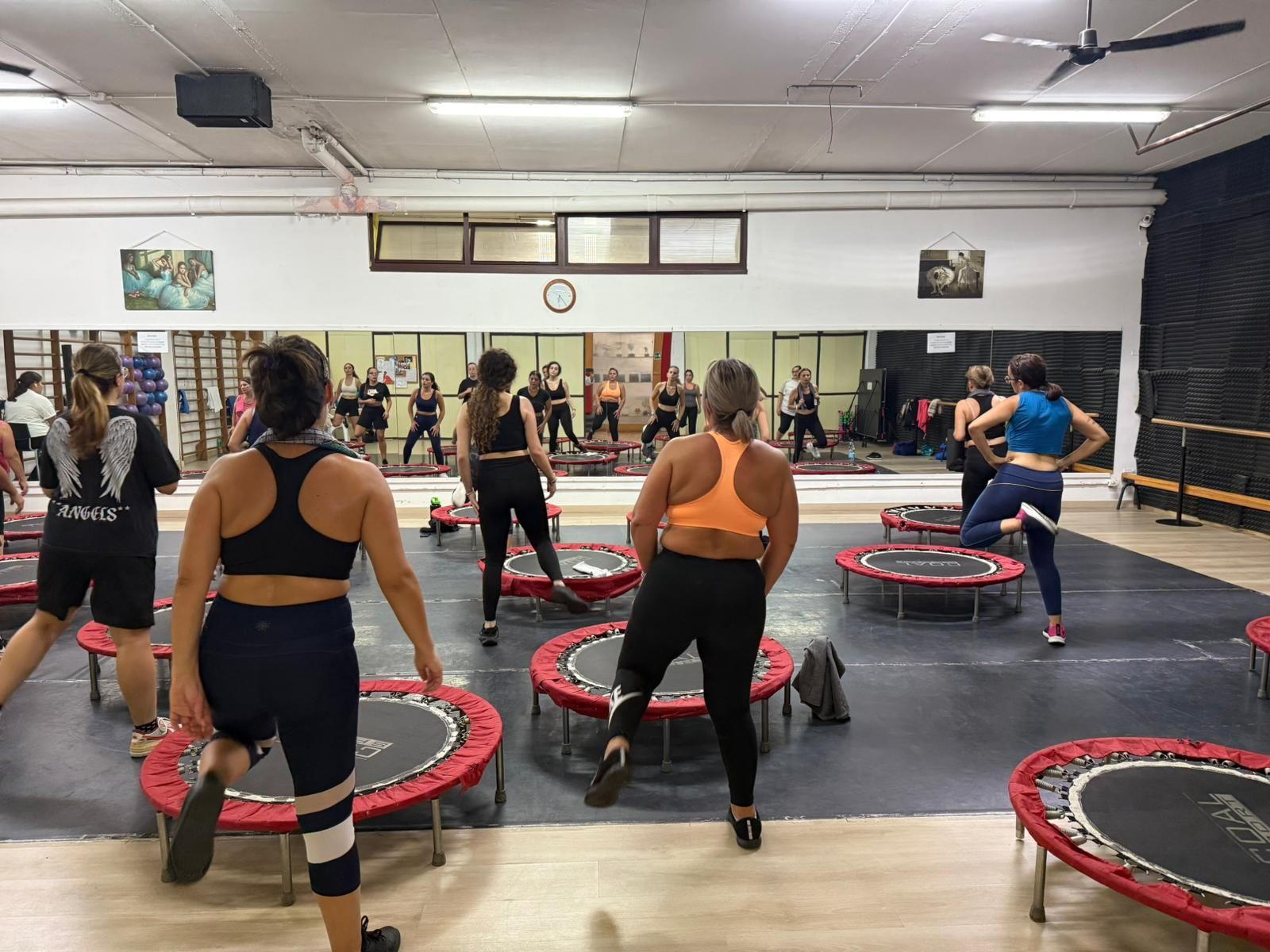Persone che si allenano su mini trampolini in palestra. Gli specchi alle pareti riflettono l'allenamento.