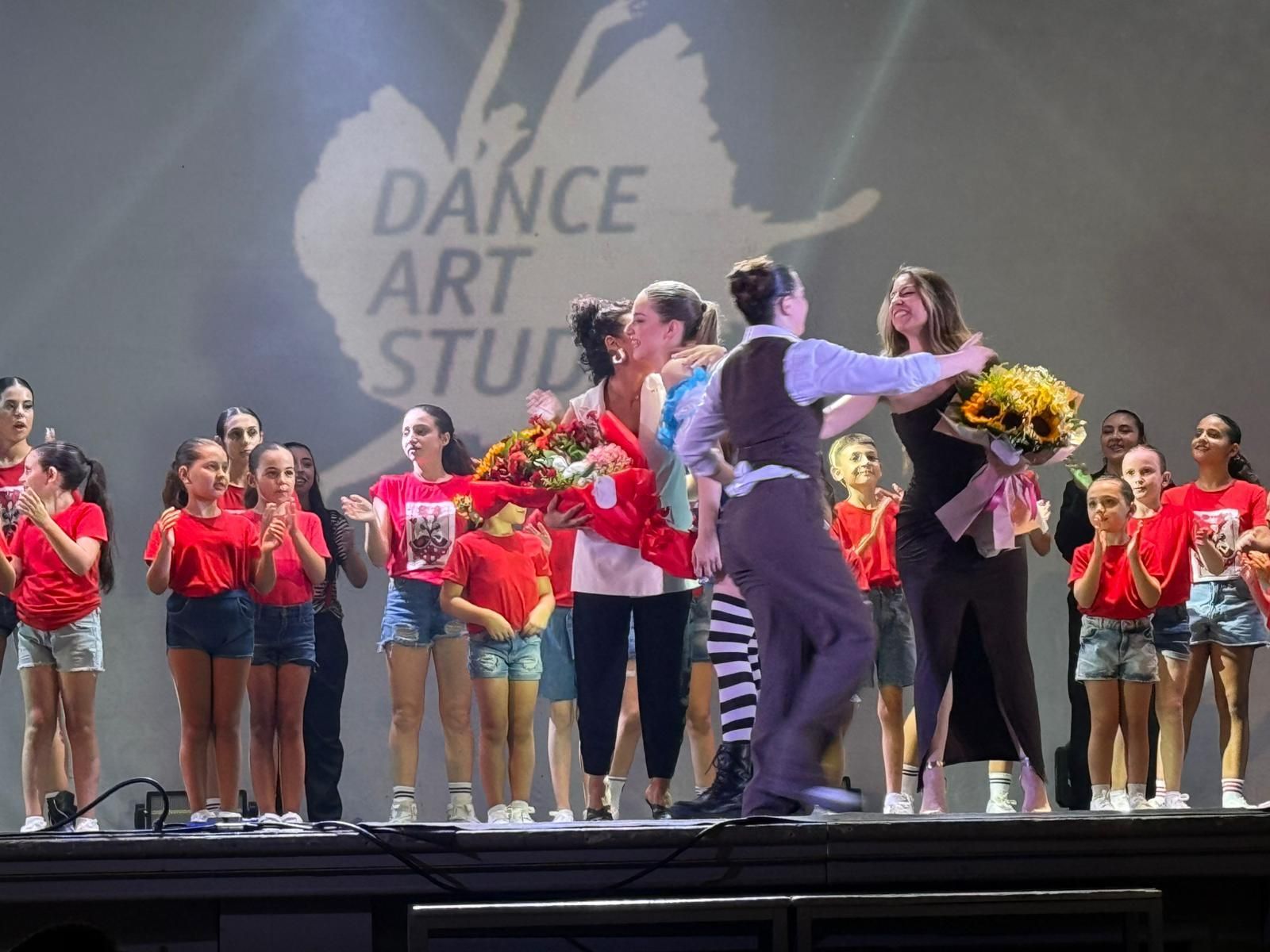 Ballerini sul palco mentre ricevono fiori. Il logo