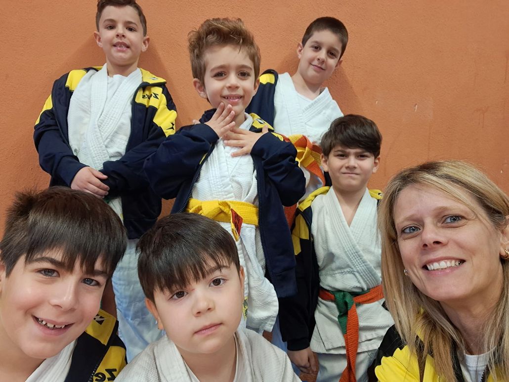 Un gruppo di bambini e una donna in uniforme da arti marziali posano per una foto, sorrisi ed espressioni felici.