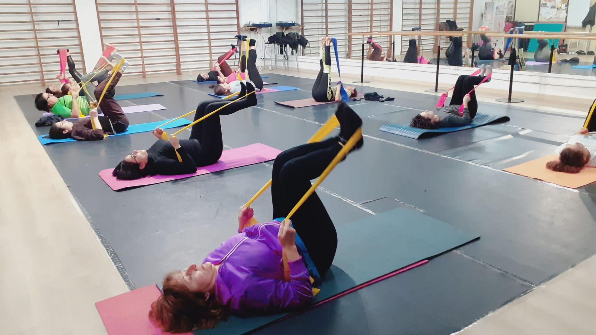 Persone su materassini che si allenano con fasce elastiche in palestra.