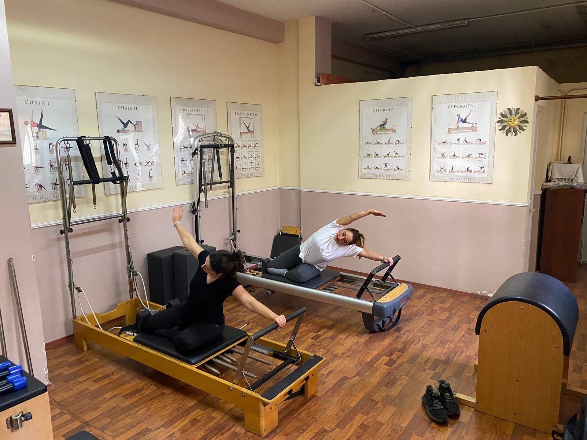 Due persone fanno pilates sui macchinari in uno studio con poster alle pareti.