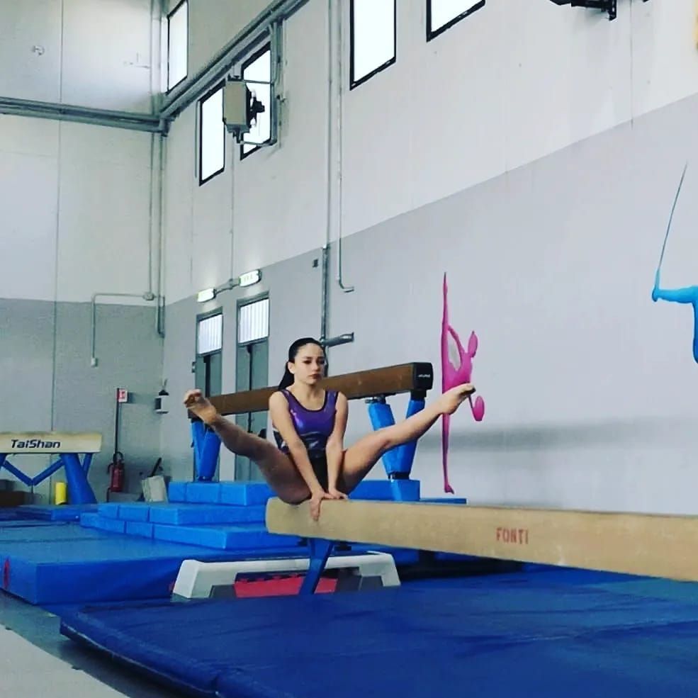 Ginnasta che esegue la spaccata su una trave di equilibrio. In palestra. Indossa un body viola.