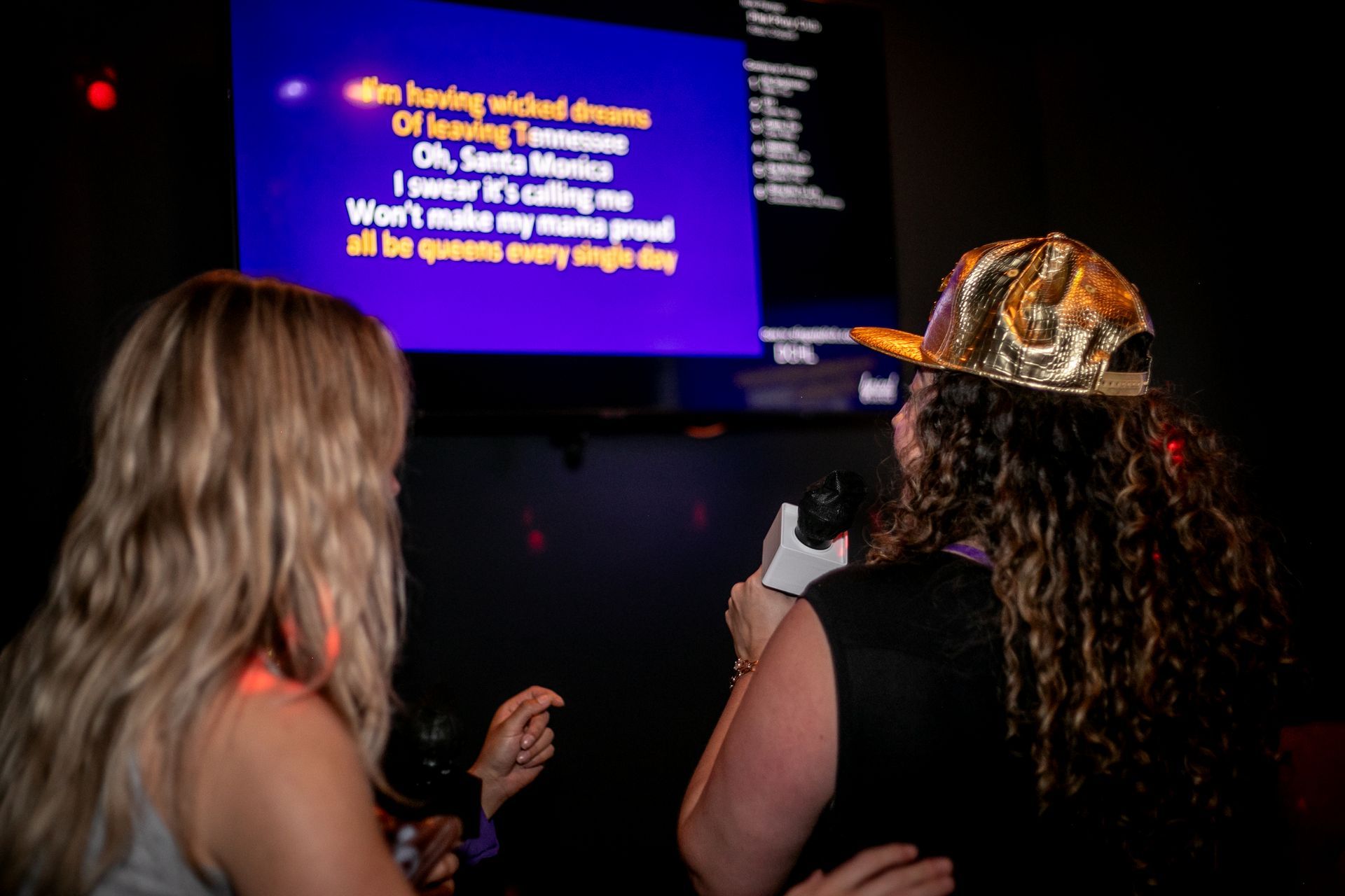 Two women singing into microphones in front of a large screen