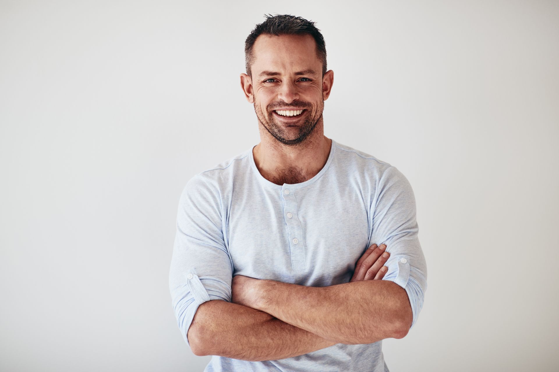 Man with crossed arms smiling. Light blue shirt, white background.