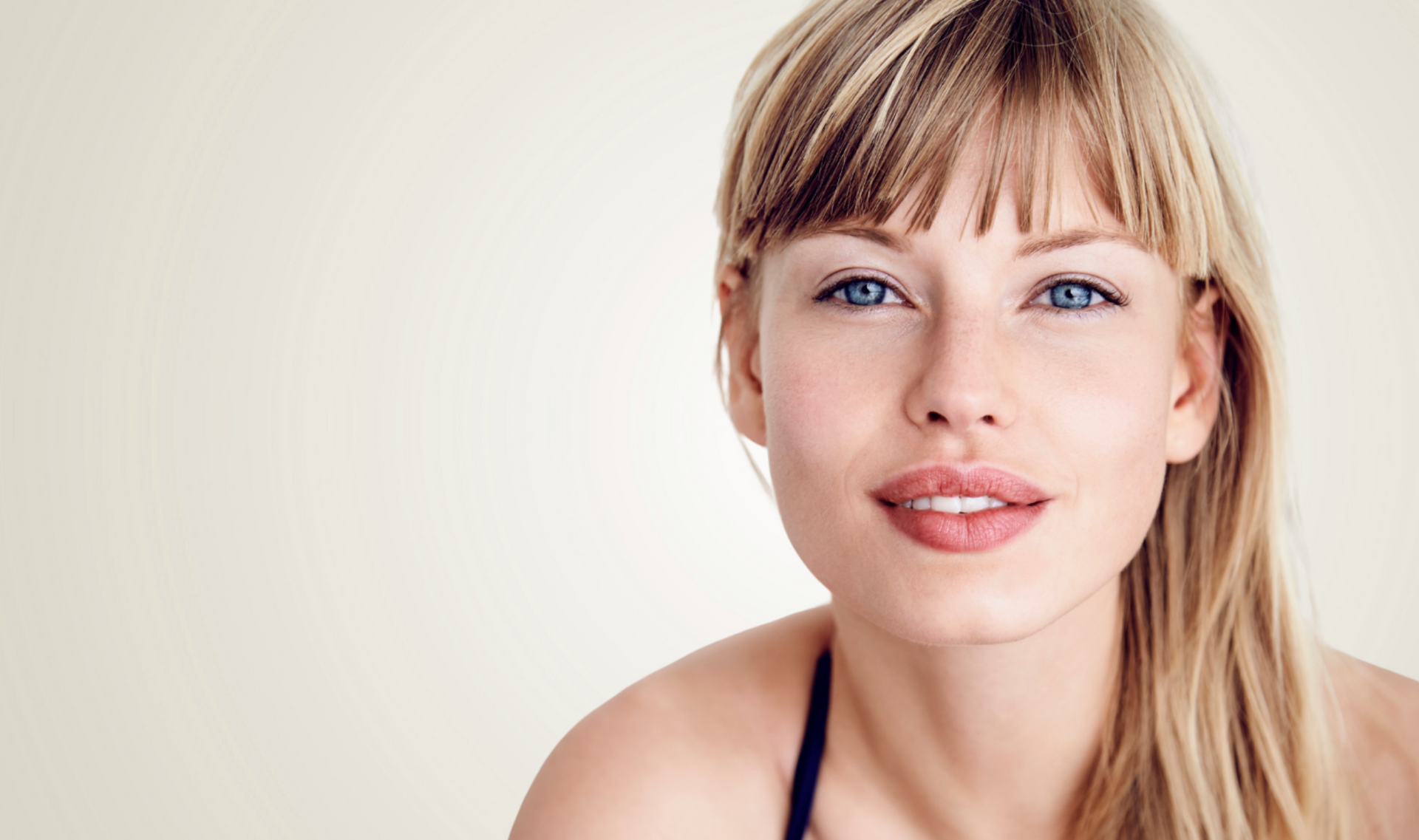 Woman with blonde hair and blue eyes, smiling, against a neutral background.