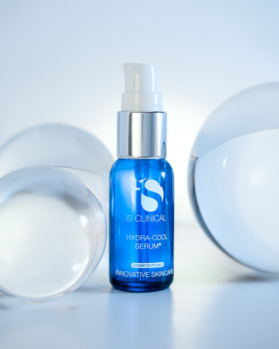 Blue iS CLINICAL Hydra-Cool Serum bottle with pump, surrounded by clear glass orbs on a light blue background.