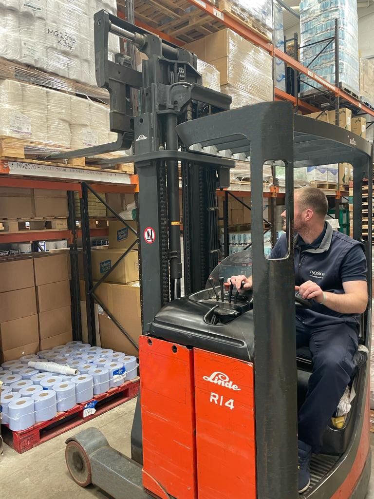 Man operating a red Linde R14 forklift in a warehouse with pallets and boxes.