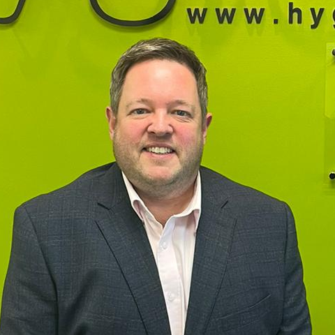 Man in a suit smiling, standing in front of a lime green wall.