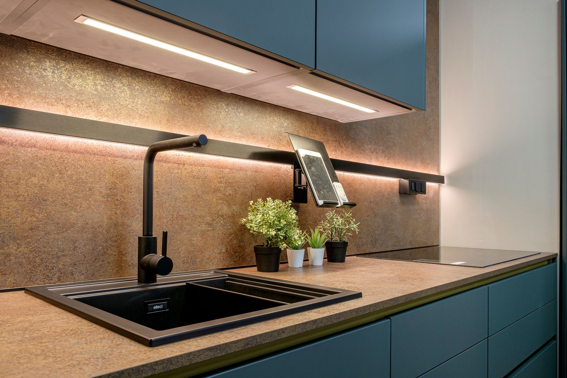 Una cucina con un lavandino, un fornello e un tablet sul bancone.