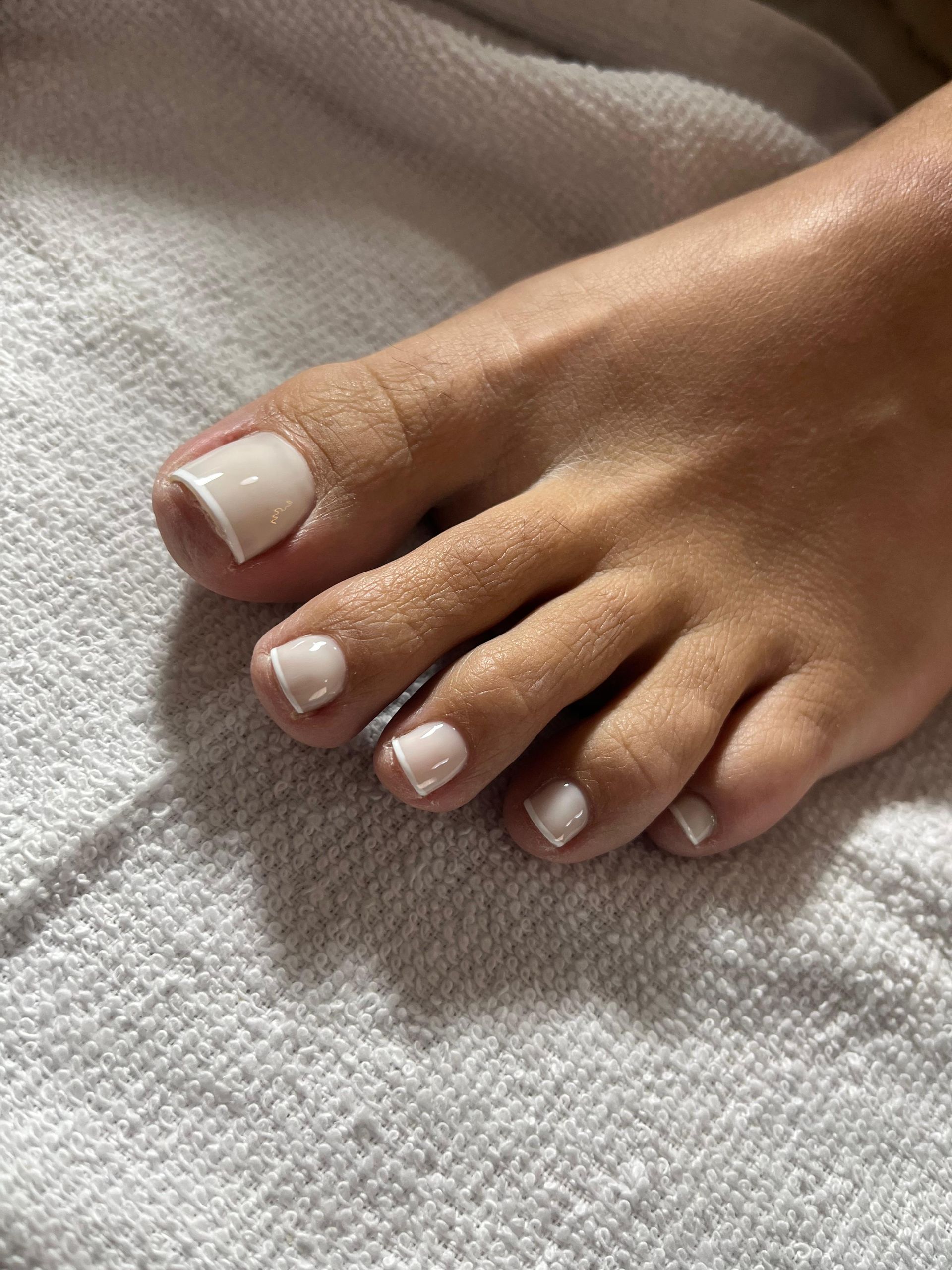 Primer plano de los dedos de los pies con manicura francesa blanca sobre una toalla blanca.