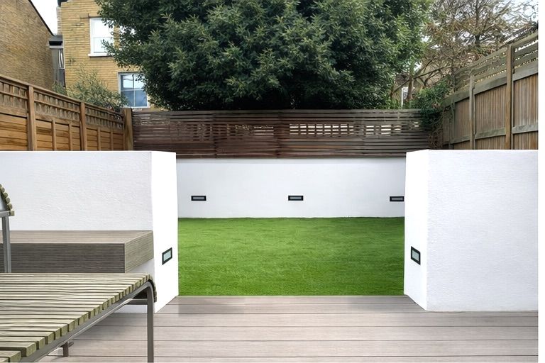 A view through white pillars onto a green lawn, surrounded by a wooden fence and large tree.