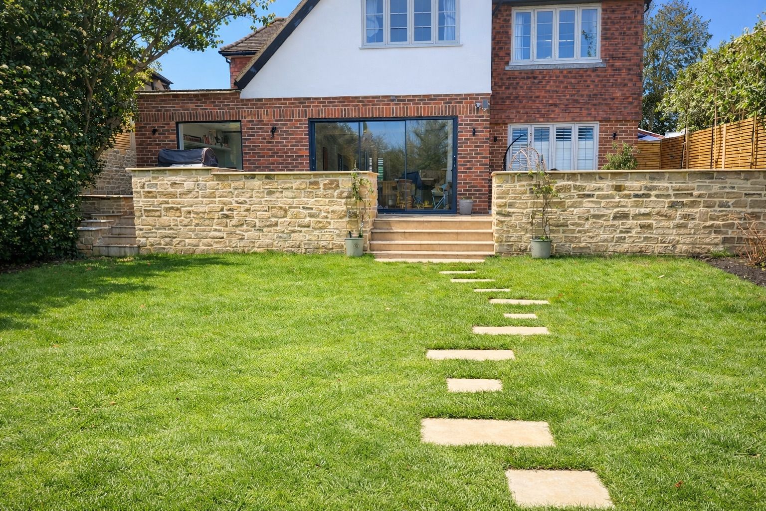 Rear yard with stone pathway leading to a house with brick and white facade; green grass and a sunny day.