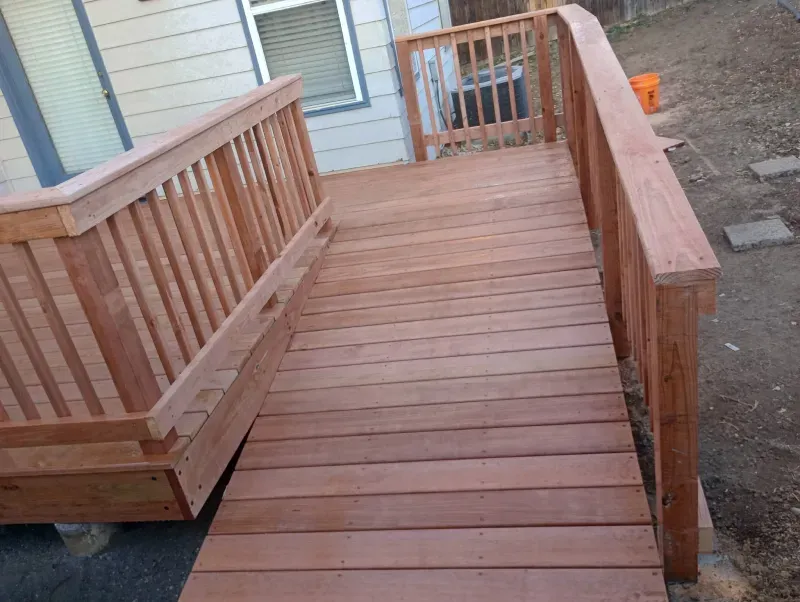 Wooden ramp with handrails leading to a deck outside a building.