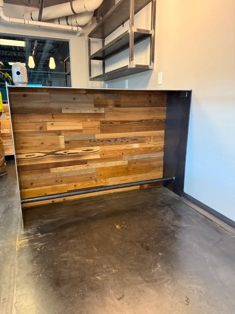 Wooden counter with metal supports and shelf in a room.