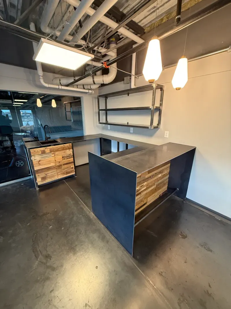 Modern office space with dark counters, wood accents, metal shelving, and pendant lights.