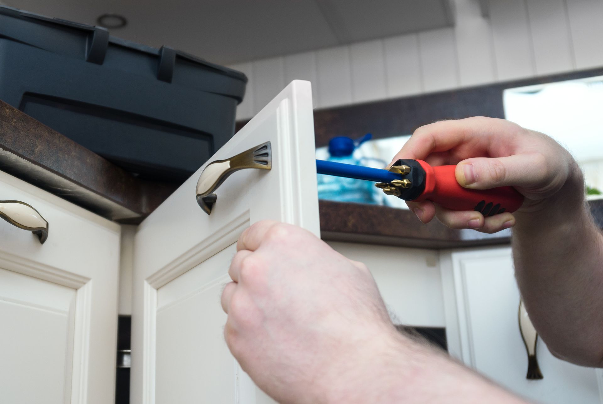 Person using a screwdriver to install a cabinet handle in a kitchen.